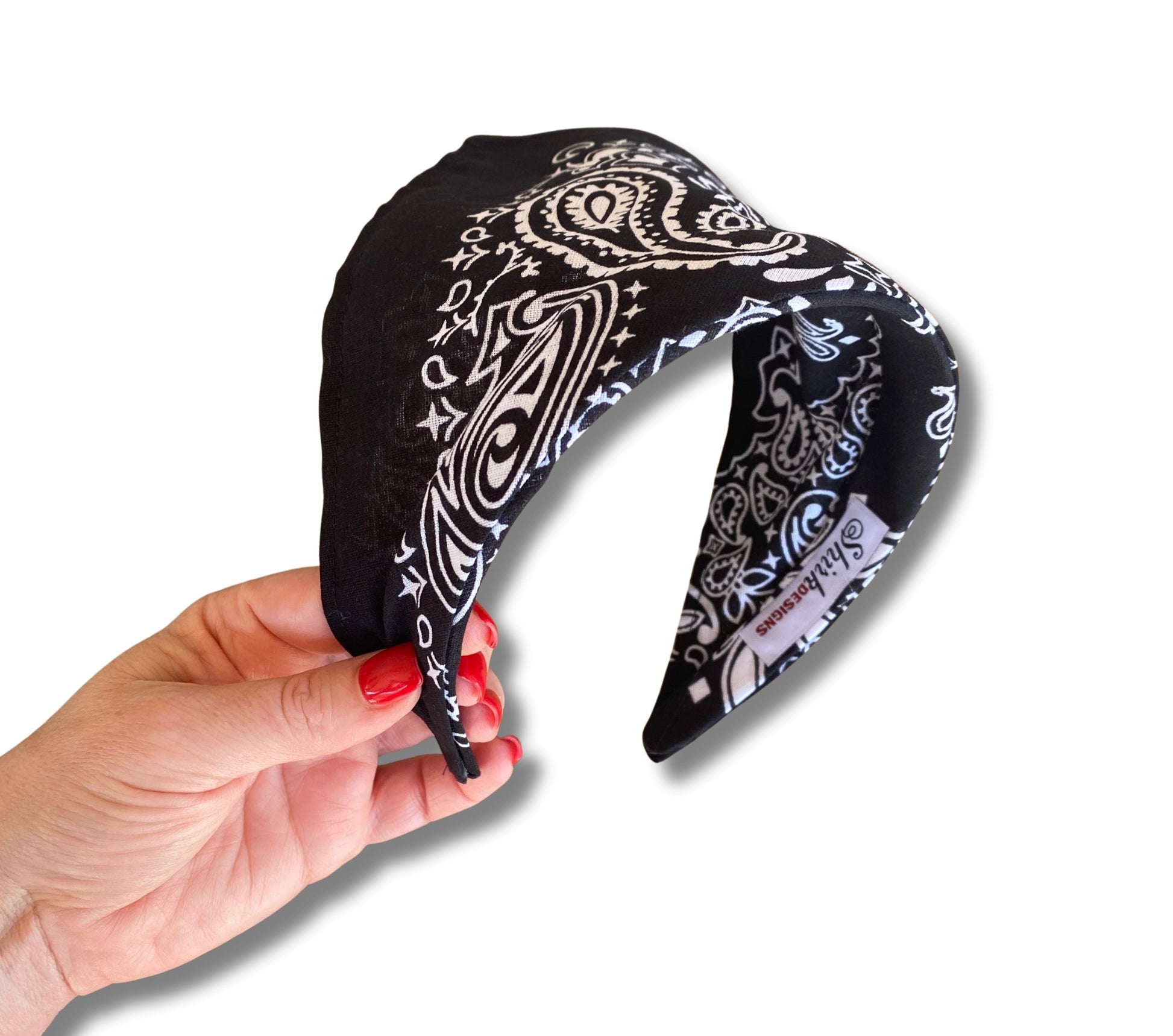 Black headband with white paisley pattern held by a hand on a white background