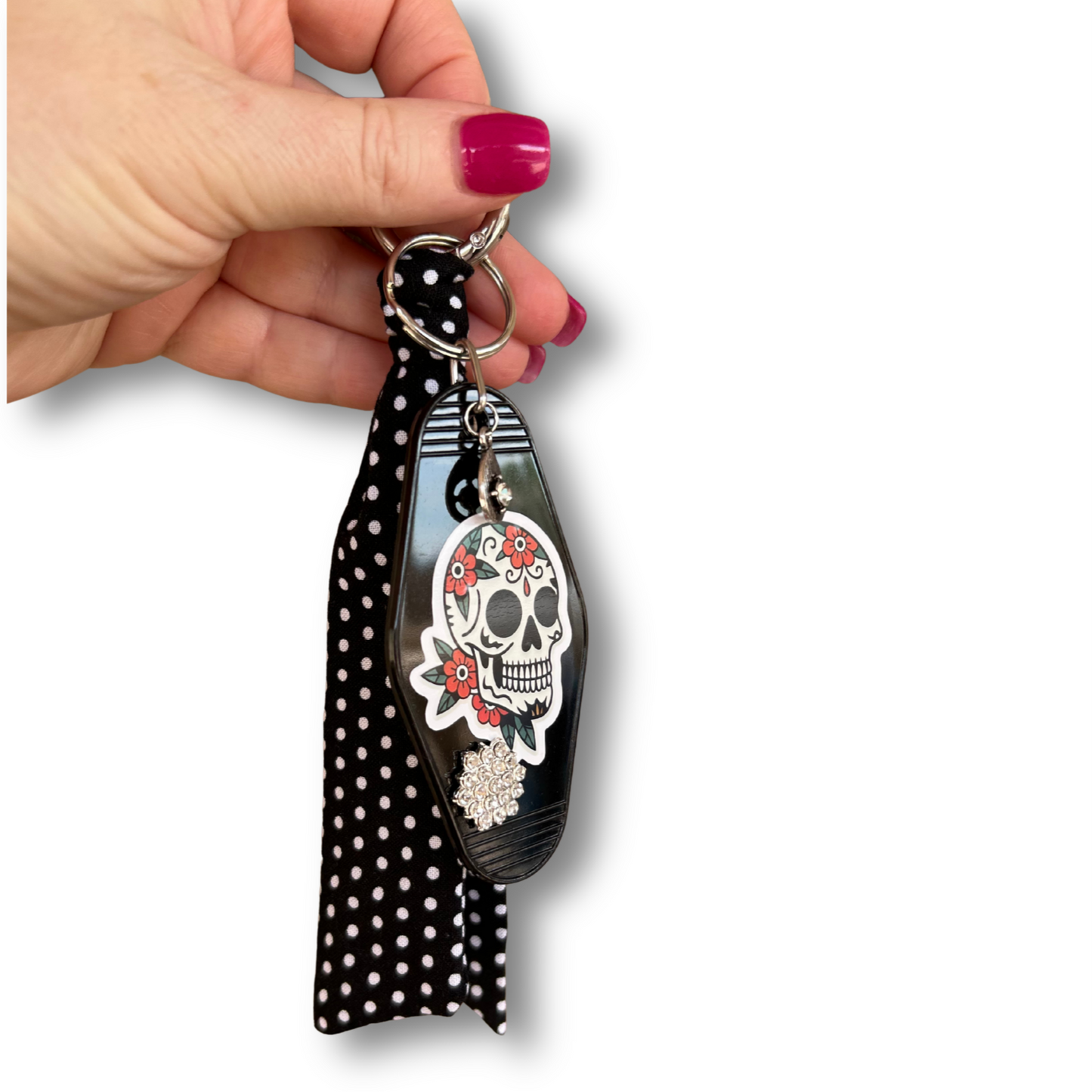 Keychain with skull design and polka dot ribbon held by a hand on a white background
