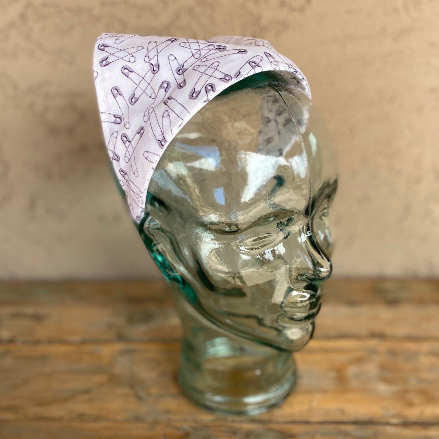Glass mannequin head with a safety pin printed no tie triangle head scarf headband.
