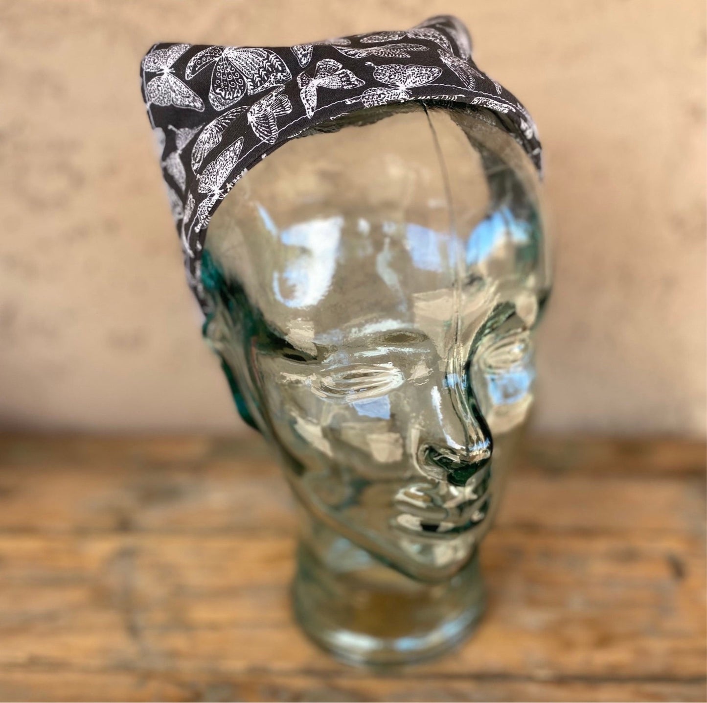 Glass mannequin head wearing a butterfly printed no tie head scarf. butterflies are white outlined and the main background is charcoal grey