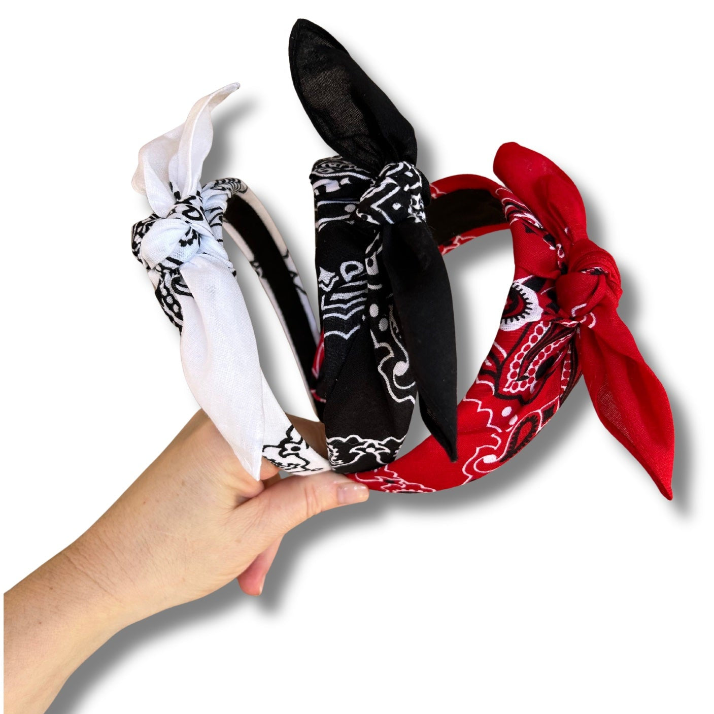 Set of bandana headbands in black, white, and red held by a hand on a white background
