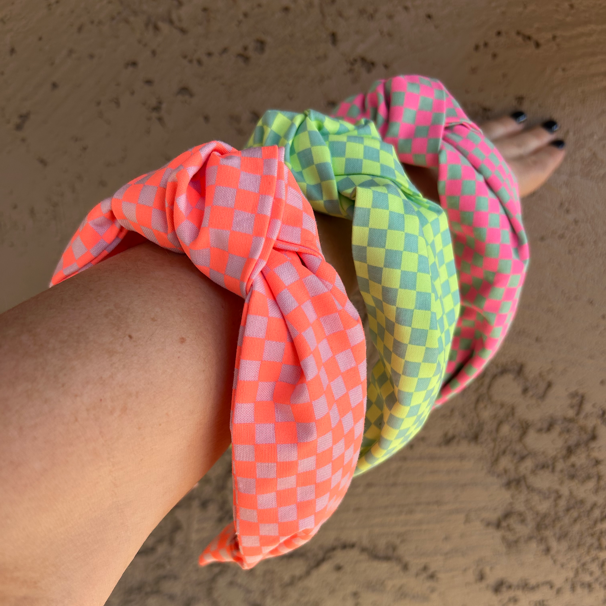 Three colorful checkered scrunchies on a person's wrist against a beige wall.