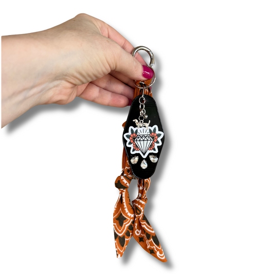 Hand holding a keychain with a cat design and orange pattern on a white background