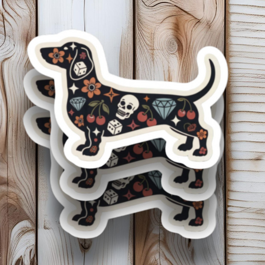 Sticker shaped like a dachshund with floral and skull designs on a wooden background.