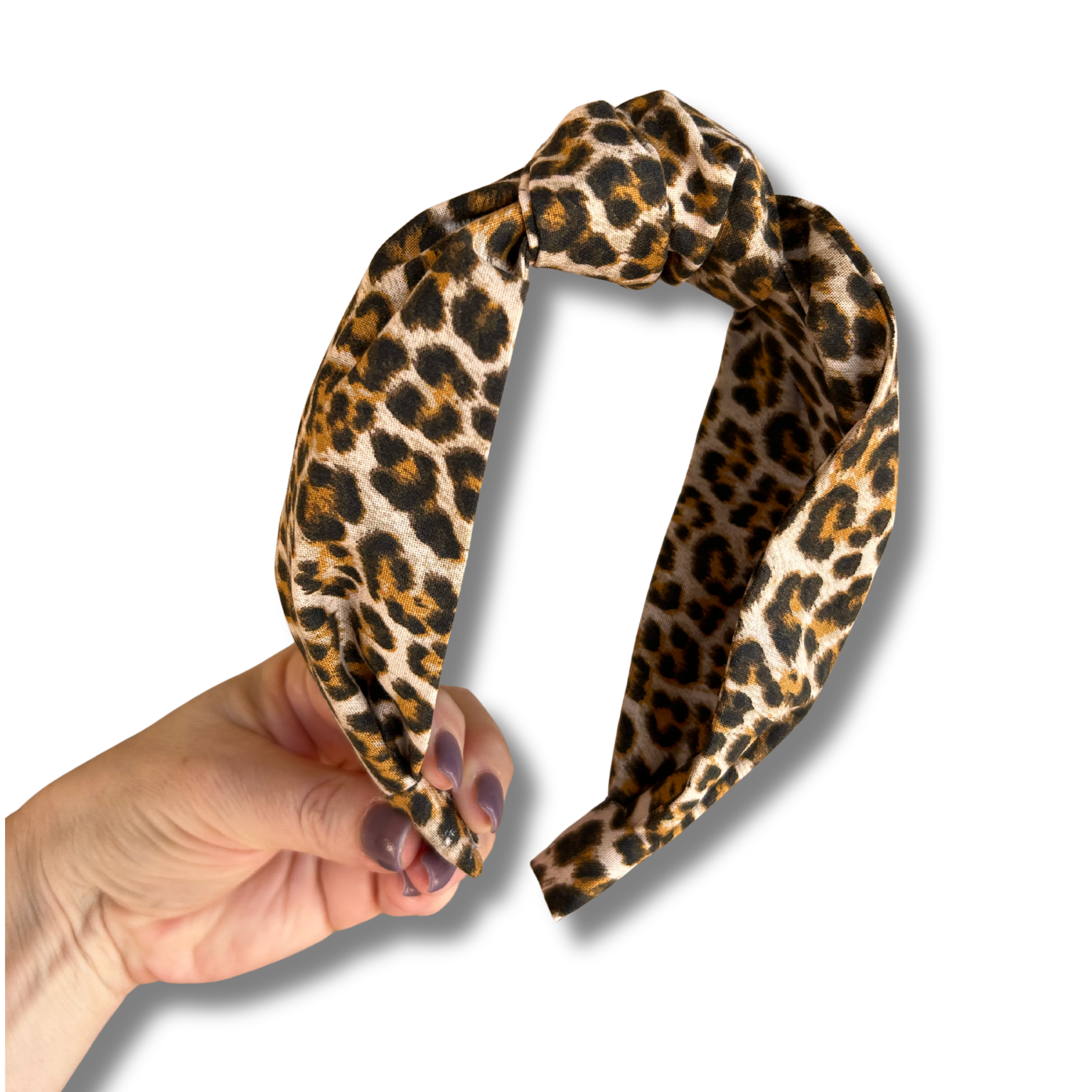 Hand holding a leopard print headband against a white background