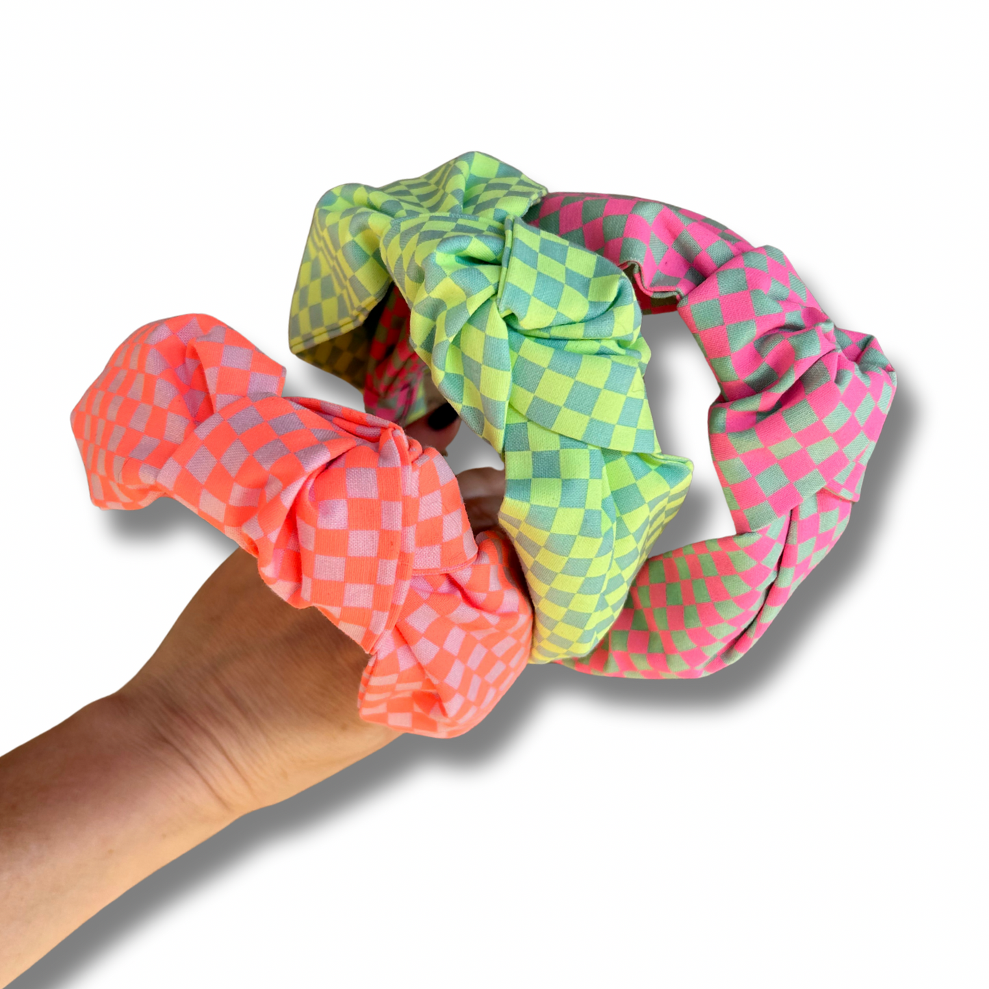 Three colorful scrunchies held by a hand on a white background