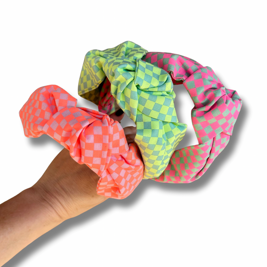 Three colorful scrunchies held by a hand on a white background