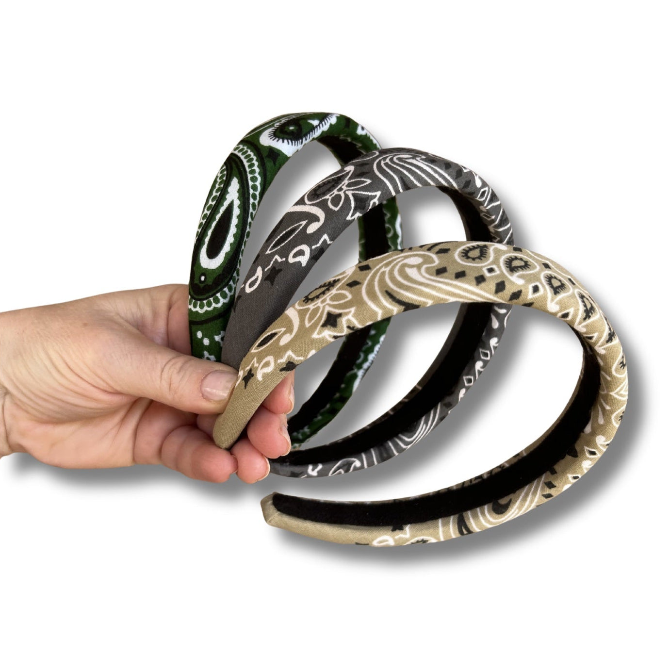 Set of three decorative headbands with intricate patterns, held by a hand against a white background.