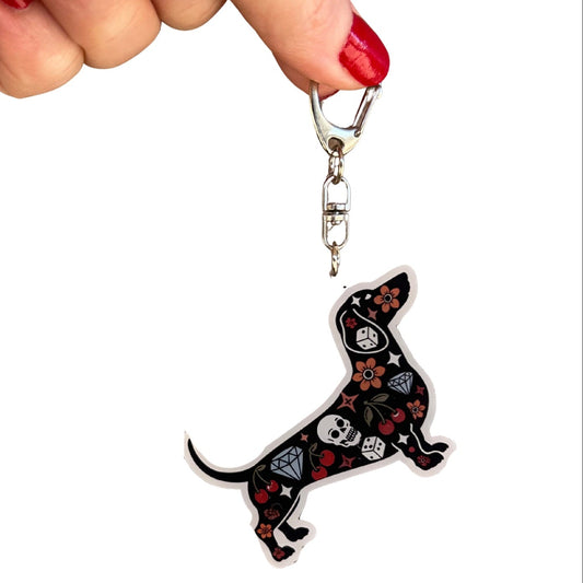 Keychain shaped like a dachshund with skull and crossbones design held by a hand.