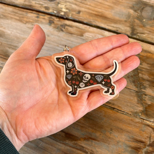 Hand holding a decorative dachshund ornament with skull patterns on a wooden surface