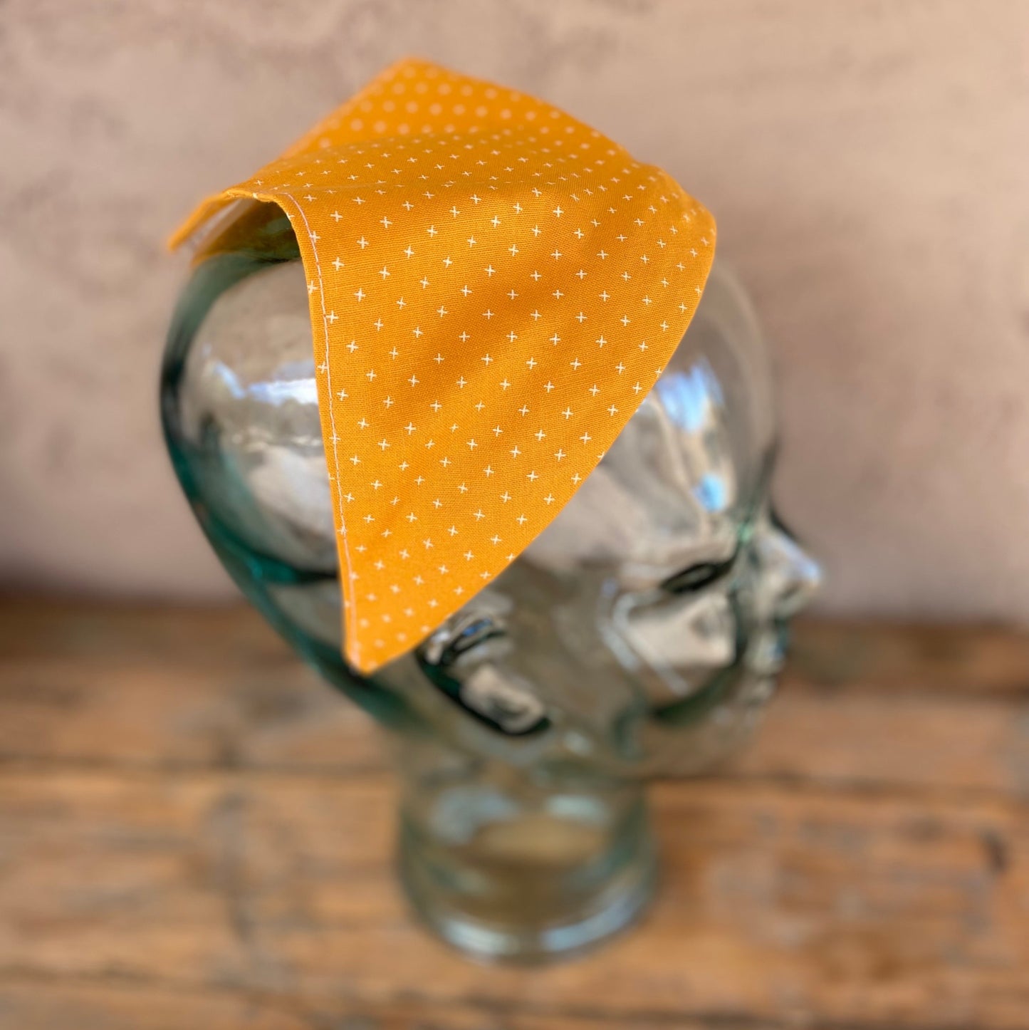 Headband that has scarf attached. It is mustard yellow with small white criss cross shapes.