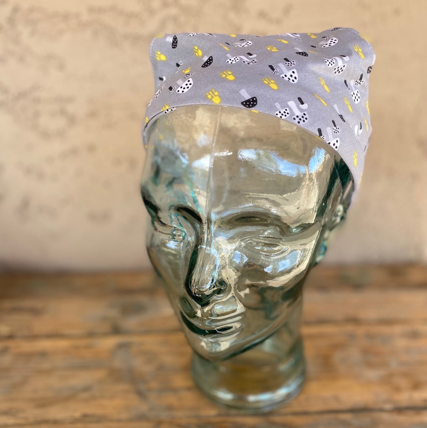 Glass head mannequin wearing a printed head scarf that has little mushrooms on it.