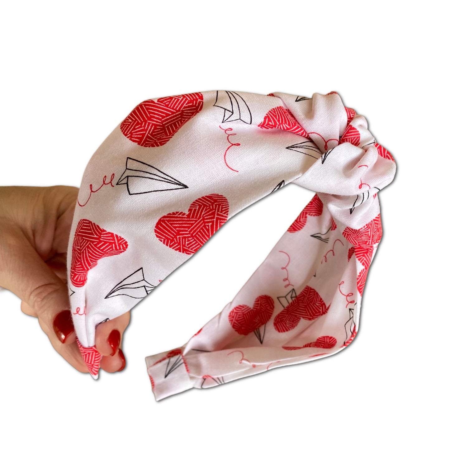 headband that has a knot at top. made with a cotton print that is white with red large hearts and paper airplane outlines