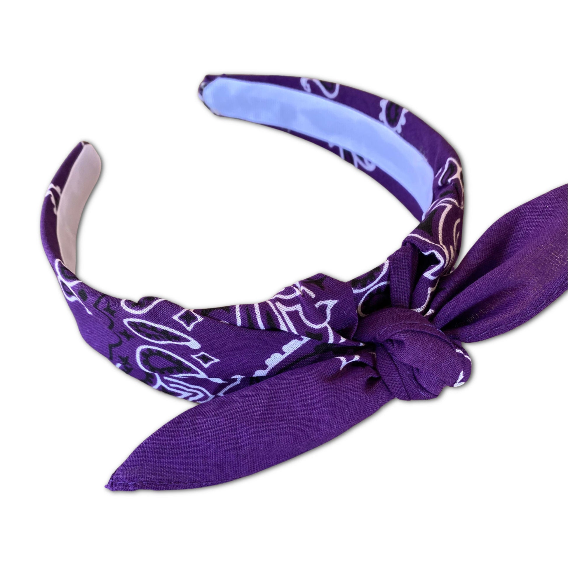 Purple paisley kerchief bandana is wrapped around a plastic headband and tied in a knot. Hairband is designed to not slip