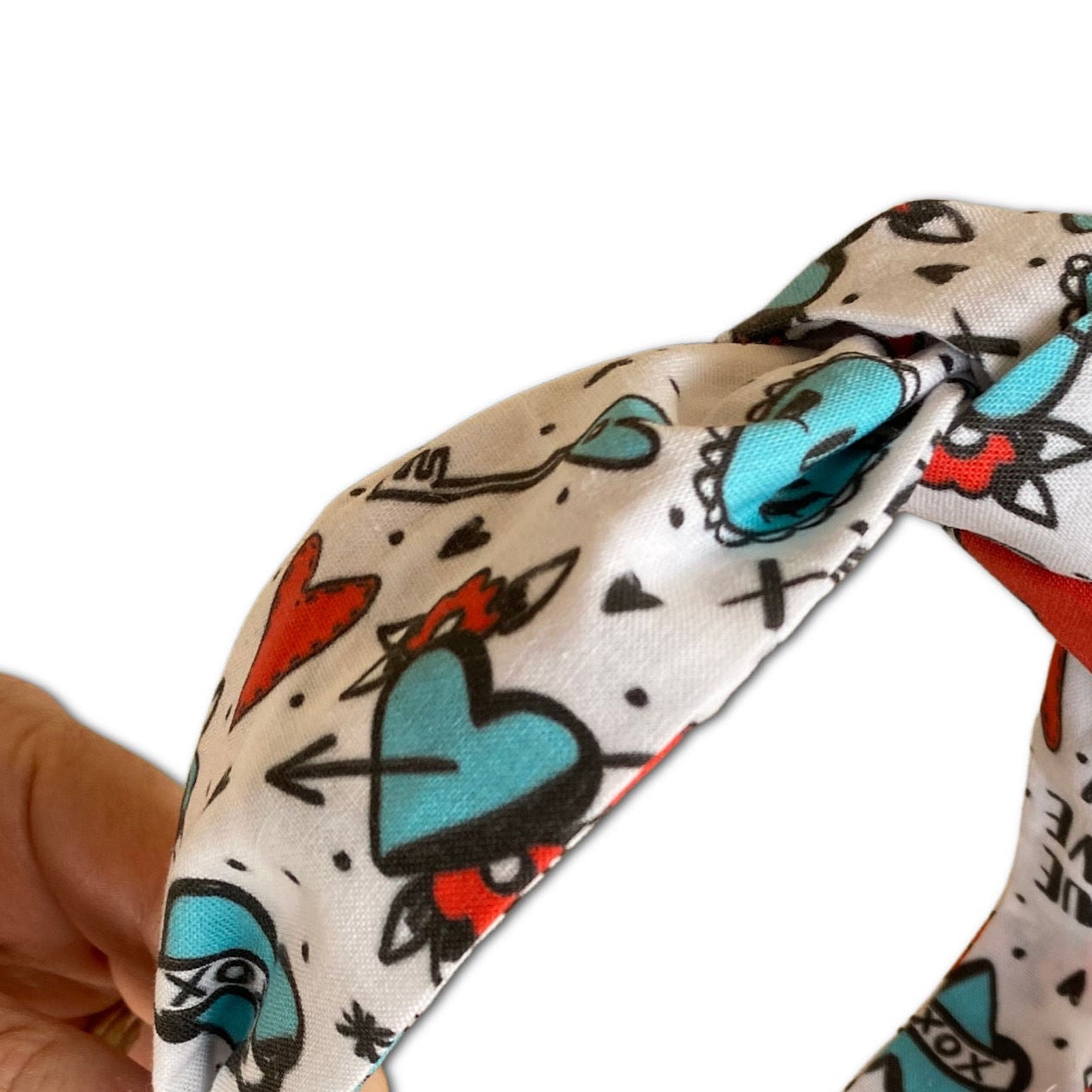 This is a headband with a knot at top. Fabric is a tattoo print with hearts, keys and locks.  Red and Turquoise colors and a white background.