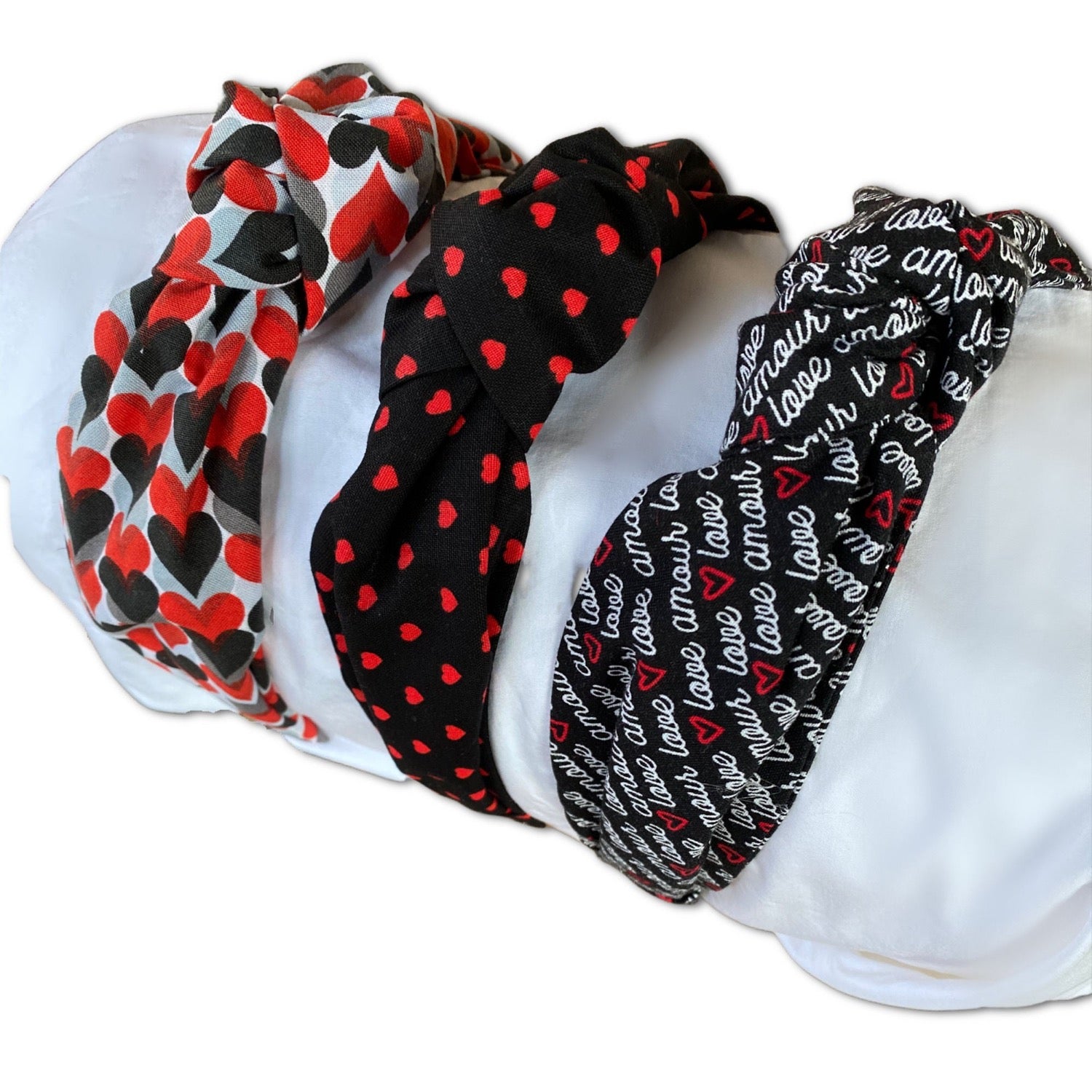Various printed Valentine's Day themed top knot styled headbands with hearts and the words love featured on one. Black, red, grey and white themed
