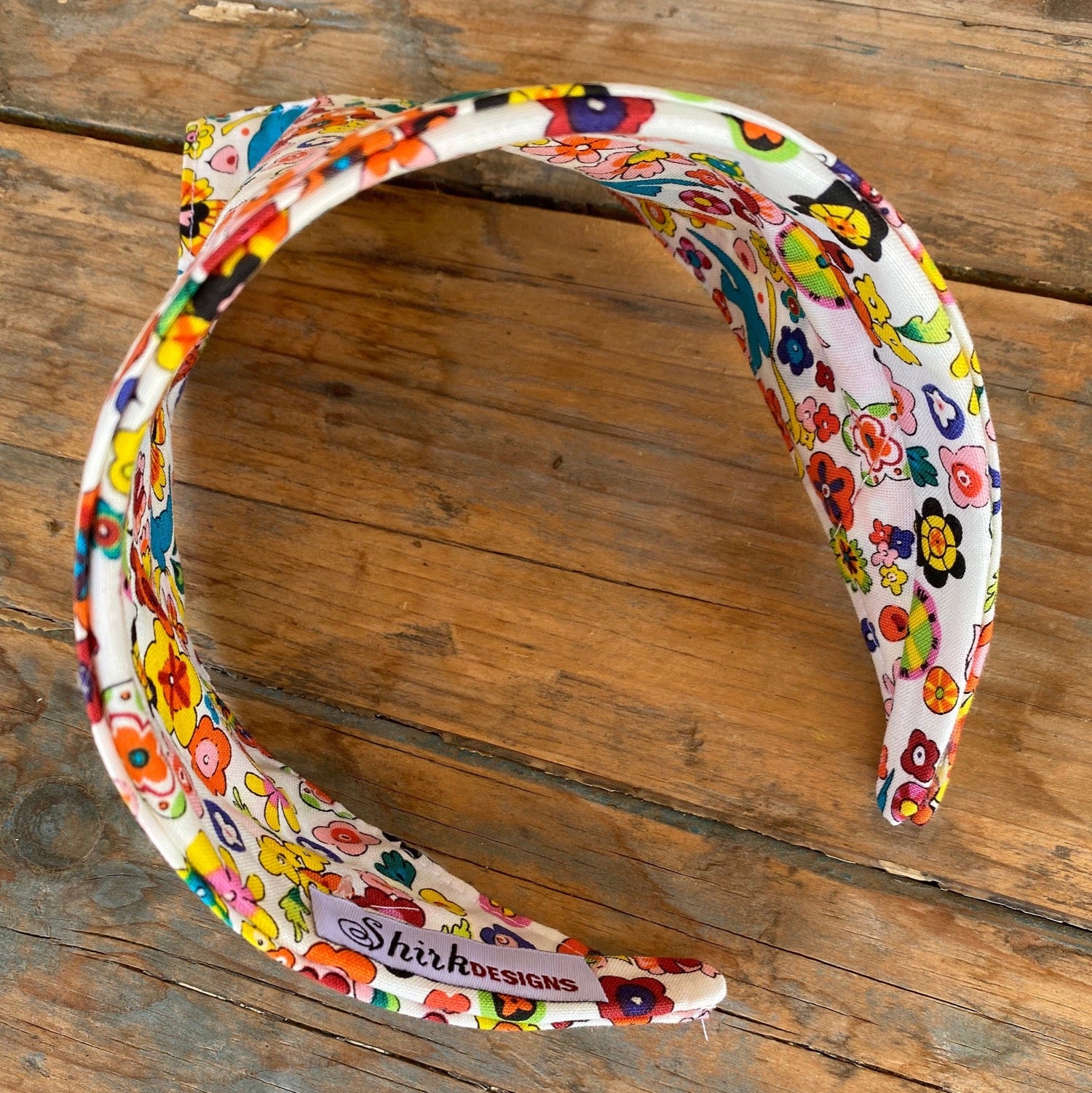Inside angle of Head scarf that features brightly colored flowers and sparrow birds throughout the print. Has a white background. The scarf has been added to a headband for easy no-tie styling.