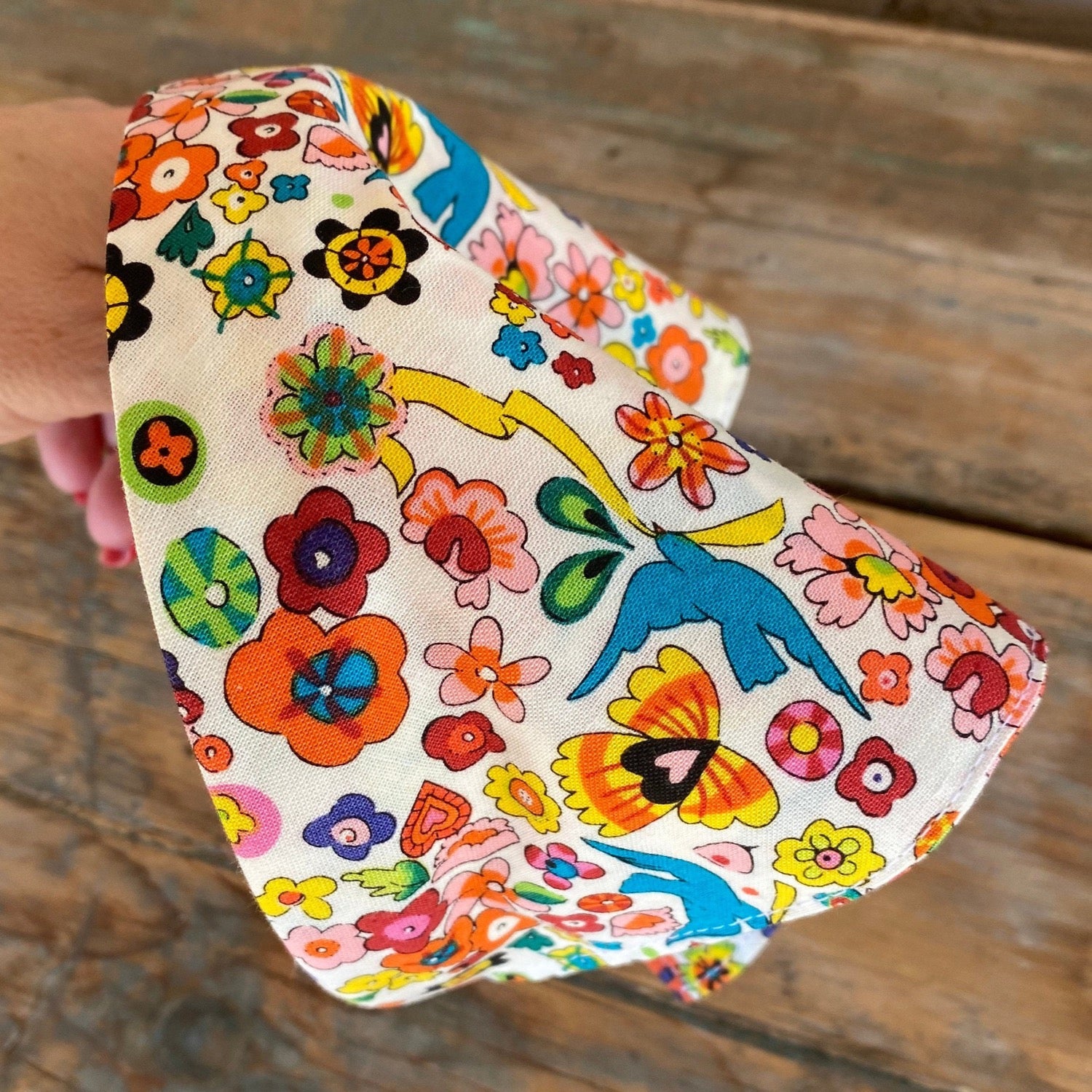 Close up of Head scarf that features brightly colored flowers and sparrow birds throughout the print. Has a white background. The scarf has been added to a headband for easy no-tie styling.