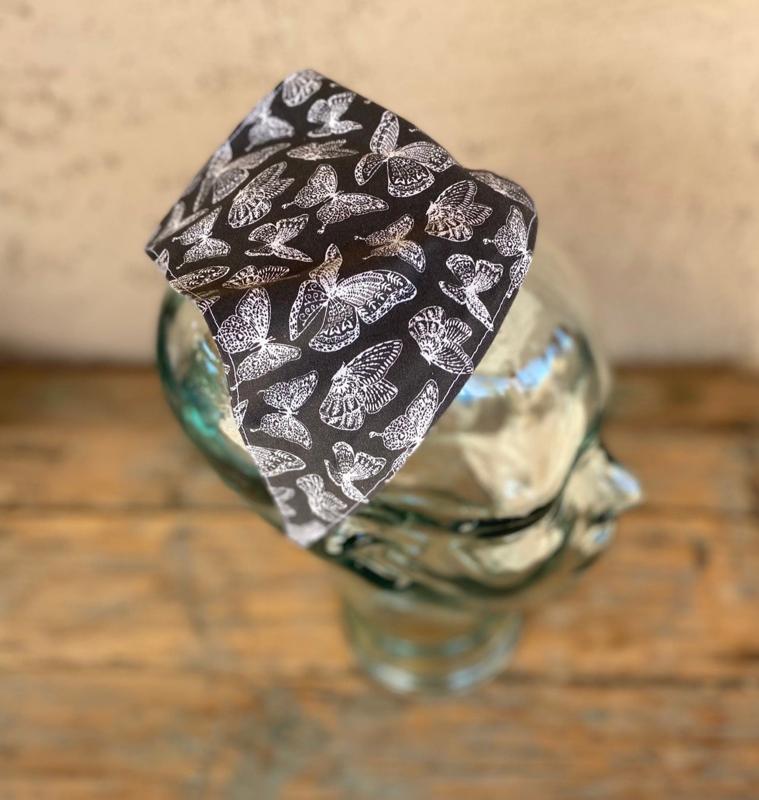 Glass mannequin head wearing a butterfly printed  no tie head scarf. butterflies are white outlined and the main background is charcoal grey