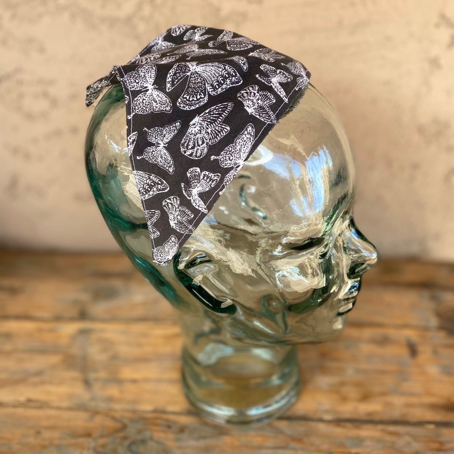 Glass mannequin head wearing a butterfly printed  no tie head scarf. butterflies are white outlined and the main background is charcoal grey